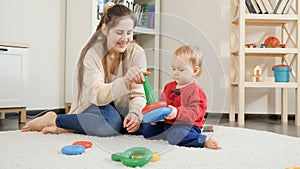 Happy babyboy with mother playing with colorful toys on carpet in living room