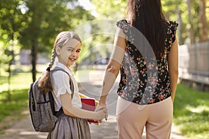 Happy back to school. Back view of mother and cute daughter holding hand while walking to school along city street.