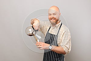 Happy bald barista man is pouring come coffee from chemex coffeemaker.