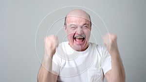 Happy bald senior man celebrating his success over gray background.