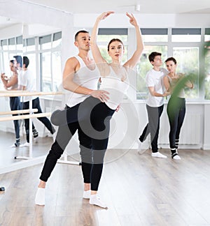 Happy ballet couple partners preparing in rehearsal for contest, training ballet poses with support in classroom