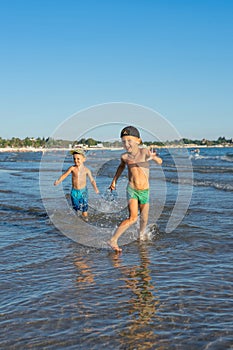 Happy barefoot family having fun Ã¢â¬â two brothers together run with splashes by water pool along surf of sunset sea beach. Active