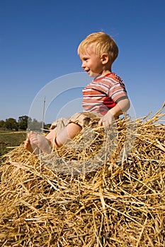 Happy barefooted baby boy sit on a hayrick