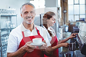 Happy barista smiling at camera and holding a cup of coffee