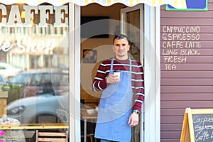 Happy barista standing at cafe entrance, portrait of mature business man attend new customers in his coffe shop photo
