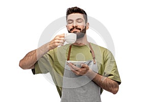 Happy barista or waiter in apron drinking coffee