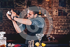 happy barman using shaker for cocktail preparation. Portrait of barman making tequila based margarita at local pub