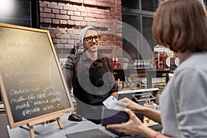 Happy barman and woman paying money at cafe