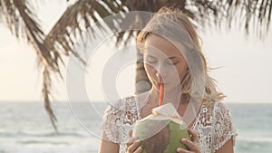 Happy beach bikini woman relaxing drinking fresh coconut water lying down sunbathing on fun Caribbean vacation