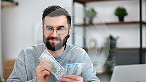 Happy bearded business man in eyeglasses counting cash money dollar currency banknote at workplace