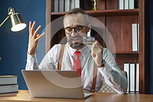 happy bearded business man holding credit card and using laptop computer typing on keyboard enter code for Online shopping from