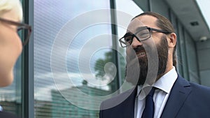 Happy bearded businessman looking at female colleague, discussing successful job