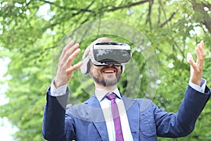 Happy bearded businessman in suit uses virtual reality glasses outdoor. Future technology concept