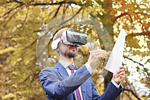 Happy bearded businessman with virtual reality glasses signs documents in autumn park. Electronic signature, Future technology or