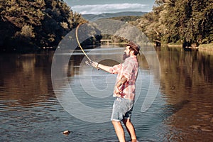 Happy bearded fisher in water. Fishing on the lake at the morning. Gone fishing. Fisherman with rod and fish. Set up rod