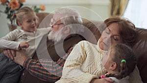 Happy bearded grandfather and sweet grandmother hugging and talking with their small funny granddaughters