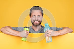 happy bearded man behind paper hold fitness barbell and water bottle for spot training, health.
