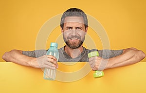 happy bearded man behind paper hold fitness barbell and water bottle for spot training, health.