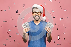 Happy Bearded man in casual and christmas hat holding money and looking at the camera isolated over pink background