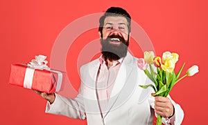 Happy bearded man with gift box and bouquet of tulips. Spring flowers and gift. Present box. Bouquet of flowers