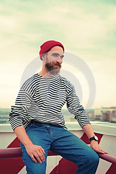 Happy bearded man in red hat smiling while sitting on the roof