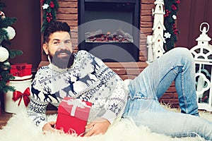 Happy bearded man resting near fireplace at Christmas. Man in knitted sweater sitting in front of the chimney. Guy holds christmas