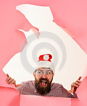 Happy bearded man in Santa hat looking through paper hole. Smiling guy in checkered shirt making hole in paper. Winter