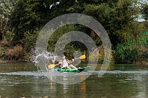 Happy bearded man in shirt and cap kayaking at the river with splashes. Copy space. The concept of watersport