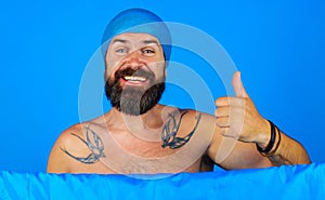 Happy bearded man in shower cap on head shows thumb up. Bath time. Showering and washing. Good mood.