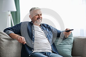 Happy bearded senior man watching TV at home