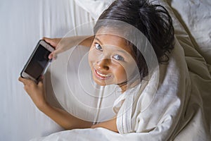 Happy and beautiful 7 years old child having fun playing internet game with mobile phone lying on bed cheerful and excited in