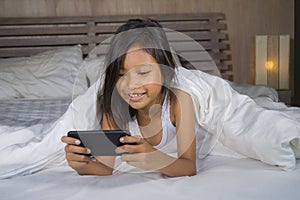 Happy and beautiful 7 years old child having fun playing internet game with mobile phone lying on bed cheerful and excited in