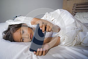 Happy and beautiful 7 years old child having fun playing internet game with mobile phone lying on bed cheerful and excited in