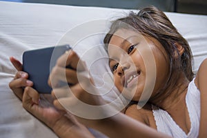 Happy and beautiful 7 years old child having fun playing internet game with mobile phone lying on bed cheerful and excited in