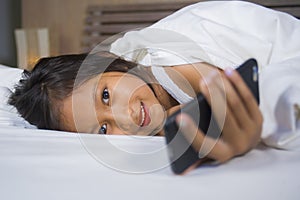 Happy and beautiful 7 years old child having fun playing internet game with mobile phone lying on bed cheerful and excited in kid