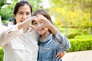 Happy beautiful asian adult woman and cute child girl forming a heart with their hands while hugging and smiling in garden,love of