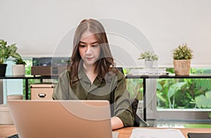 Happy beautiful Asian business woman sitting using laptop computer for working at desk in private office