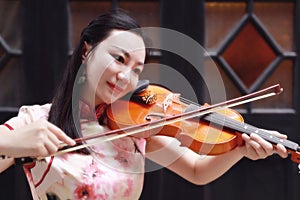 Happy beautiful Asian Chinese woman artist in traditional chi-pao cheongsam play violin in a garden close-up