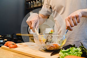 Happy beautiful asian man prepare salad food in the kitchen. Young asian male cooking healthy food while staying at home.