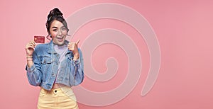 Happy beautiful Asian teen shopaholic women showing credit card and her finger pointing isolated on pink background