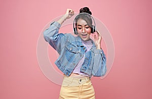 Happy beautiful Asian teen woman in yellow glasses listening music in headphones and dance on pink background