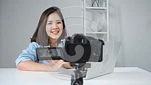 Happy beautiful Asian woman answer question from her subscribers. Female blogger recording video with laptop from camera to