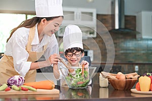 Happy beautiful Asian woman and cute little boy with eyeglasses prepare to cooking in kitchen at home. People lifestyles and