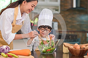 Happy beautiful Asian woman and cute little boy with eyeglasses prepare to cooking in kitchen at home. People lifestyles and