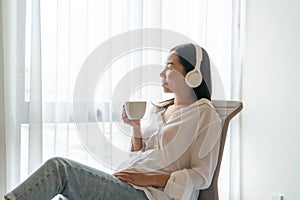 Happy beautiful Asian woman drinking coffee and listening music while sitting at home. Lifestyle, leisure activities on weekend