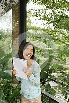 Happy Beautiful Asian Woman holding book or diary on green natural outdoor background