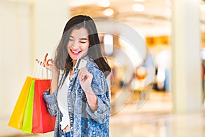 Happy beautiful Asian woman smile at credit card, hold shopping bags. Shopaholic people, retail special offer price concept