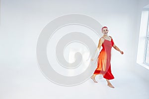 Happy beautiful bald woman with red hair meloman in long red dress raising arms photo