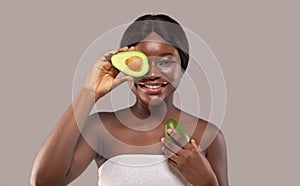 Happy beautiful black female holding fresh ripe green avocado half near eye