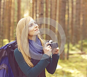 Happy, beautiful blond girl taking pictures in forest. Camp, tourism, hiking concept.